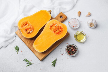 Butternut squash cut in half on a wooden board with garlic oil pepper salt and rosemary