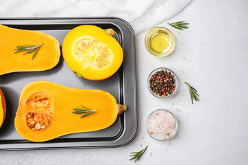 Halved butternut squash with rosemary, oil, peppercorns, and salt on a baking tray.