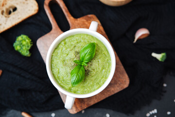 Creamy green broccoli soup served in white bowl with basil garnish on rustic wooden board
