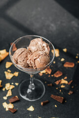 Glass cup with scoops of chocolate ice cream and waffle crumbs on dark surface