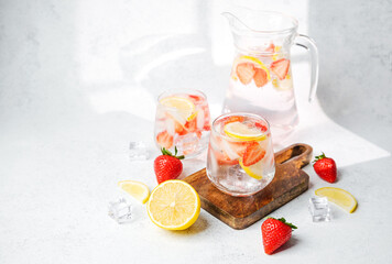 Strawberry lemon infused water in pitcher and glasses served with ice cubes and fresh fruit