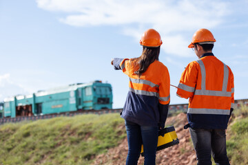 Two railway engineers in orange safety jackets observe trains on an elevated track under...