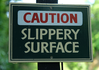 Obraz premium Close-up of a Caution Slippery Surface sign warning pedestrians of potential hazard in outdoor area.