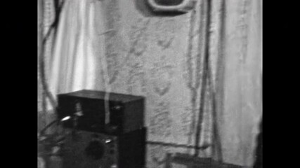 Man imitates gangster inside Soviet apartment interior. Comic parody of mafia culture with vintage criminal style, humor, nostalgic scene. Black and white retro film. Old archive. Archival 1960s