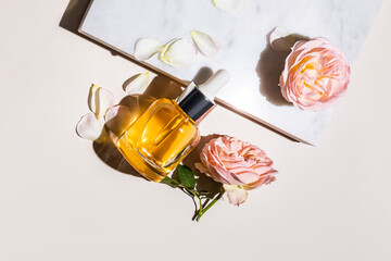 A transparent bottle with a dropper with a natural organic product, serum, oil for face and body skin care leaned on a marble podium with roses.