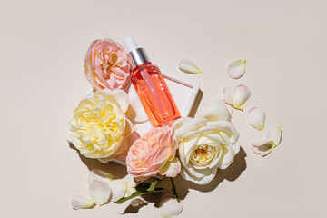 A transparent dropper bottle with a cosmetic product for face and body skin care at home on a white tray among fresh roses. Aroma product. top view.