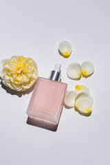 A chic cosmetic bottle with a dropper with a natural self-care product. Blank matte bottle mockup. vertical background with yellow rose and petals