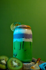 Iced green kiwi drink topped with purple taro layer, creamy foam, and lime garnish on green background.