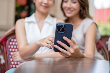 Blurred asian woman taking photos or showing phone to friend while sitting at table in front of cafe