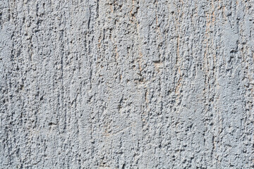 A full-frame close-up shows a rough, light gray stucco or plaster wall with an irregular and vertical pitted texture