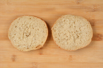 Two halves of a rustic bread roll are placed side-by-side, cut-side up, on a light brown wooden cutting board