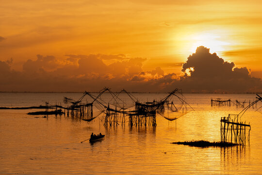 Traditional fishing nets and small boat silhouetted against vibrant sunrise at lake, showcasing local lifestyle, serene nature and cultural heritage, perfect for travel, tourism, and landscape content