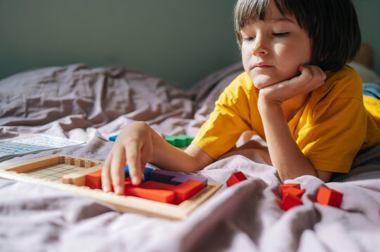 Child playing puzzle game on bed at home with focused expression