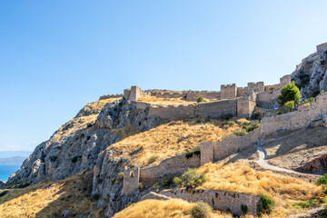 View of the medieval fortress on the slopes of Acrocorinth hill, surrounded by dry summer grass and blue sky. Historic landmark of the Peloponnese.