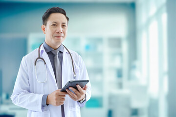 Portrait of asian senior doctor standing while using tablet in Examination Room COPY SPCAE.