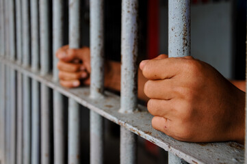 prisoner's hands behind bars with black background