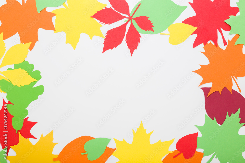 Wall mural Created colorful different paper leaves from application paper on white table background. Closeup. Autumn decoration. Empty place for text in frame. Top down view.