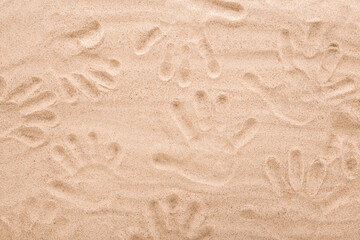 Background of people hand prints on dry light brown sea sand. Closeup. Top down view.