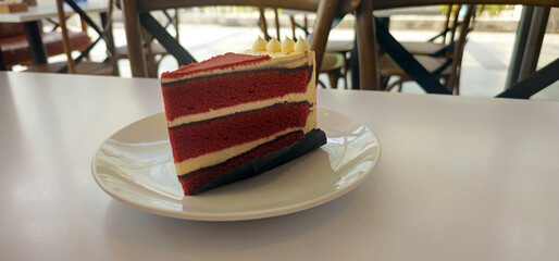 A slice of red velvet cake with cream layers on a white plate in a cozy cafe. Delicious dessert with soft texture and rich flavor, perfect for bakery, cafe, or sweet food concept.
