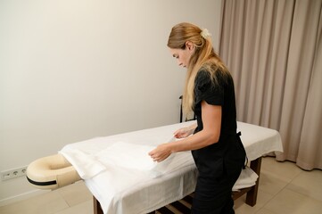 Masseuse prepares treatment room for customers in a small massage parlor during a busy working day