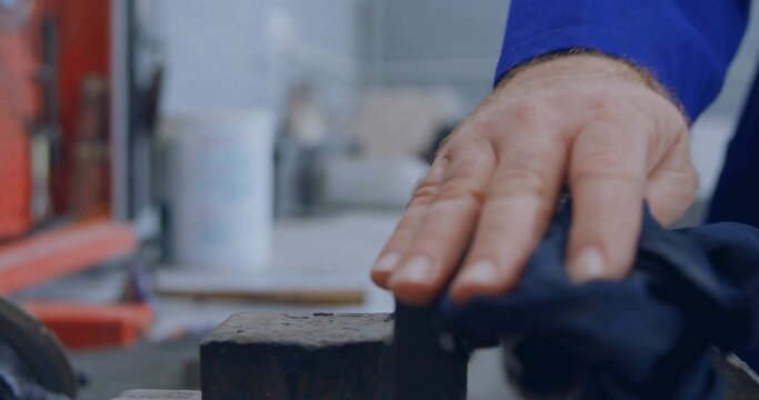 Pressing male hand in blue shirt wiping cloth against metal block on bench, with red toolbox