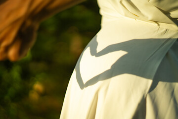 Pregnant woman makes shadow heart hands sign on belly stomach wearing white dress, close up
