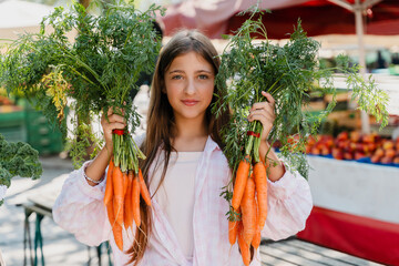 Person holding organic carrots at local market promoting sustainability