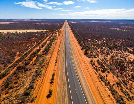 Aerial view of a straight road stretching endlessly across a flat arid landscape, blue sky - Powered by Adobe
