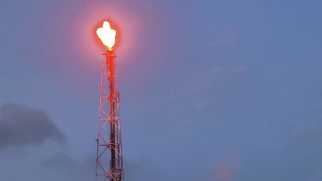 An industrial scene featuring a tall oil and gas refinery tower with a bright flare burning at its peak. This image symbolizes the complex process of extracting and managing energy resources.