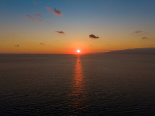 Naklejka premium Golden sunset reflecting on sea with a small boat in reflection