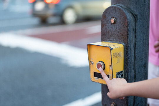 Pushing the pedestrian crossing lighting button, activate the signal for safety transportation. Close-up with selective focus on human hand.