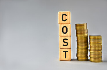 COST - word on wooden cubes on the background of stacks of coins