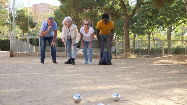 Portrait of age-diverse mature men and women standing side by side with metal boules in their hands and looking ahead at the target while playing petanque game outside in the park