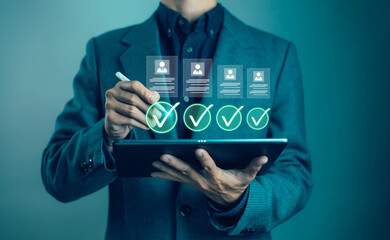 Businessman using digital tablet with holographic check mark and profile icon, representing online recruitment, human resource management, candidate selection and processes.