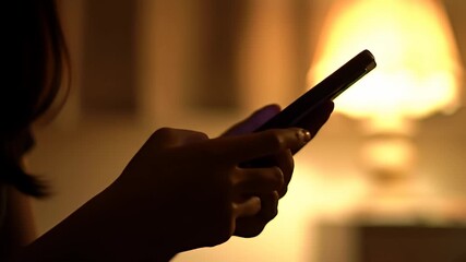 Person uses phone in dim light of lamp, focus on the phone and hands