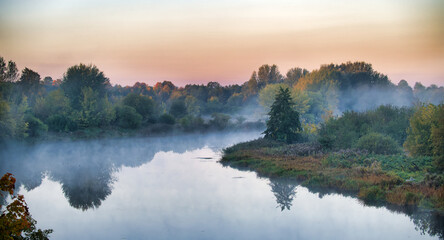 Fototapeta premium Morning mist over a calm river with trees and reflections at sunrise