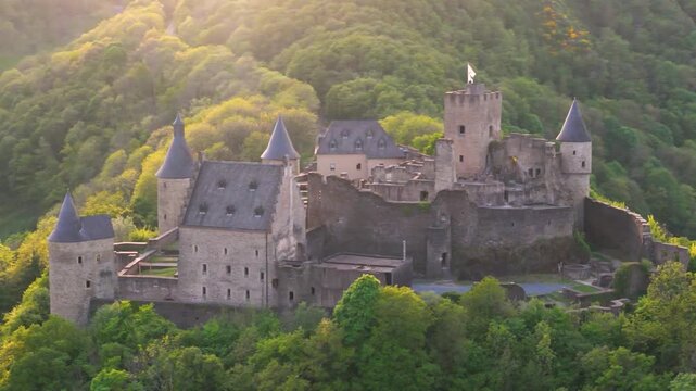 bourscheid castle ch&acirc;teau de valley green cover hills behind walls black domed towers road beside historic site surrounded by trees to left near right pans drone 