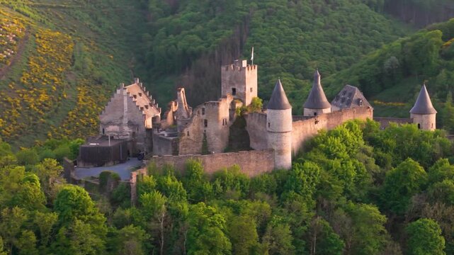 bourscheid castle ch&acirc;teau de green valley hills behind walls black domed towers flag atop foggy weather tall trees to left around right pans drone 