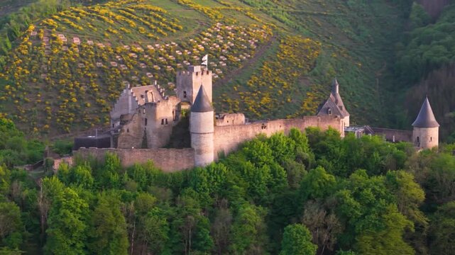 bourscheid castle ch&acirc;teau de green valley hills behind walls black domed towers flag top foggy day tall trees yellow to left near right drone panning shot 