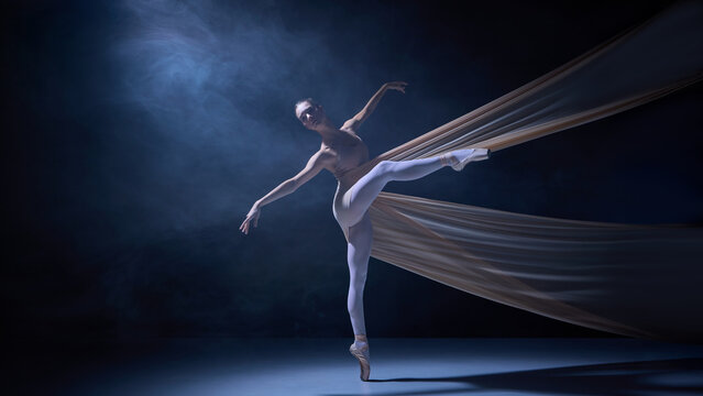 Ballet dancer standing en pointe wrapped in fabric under blue stage light. Concept of stage art, balance mastery, and precision control in classical dance photography.