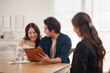 Asian couple sitting together using tablet, researching new home and family planning ideas, showing teamwork, love, and positive lifestyle.