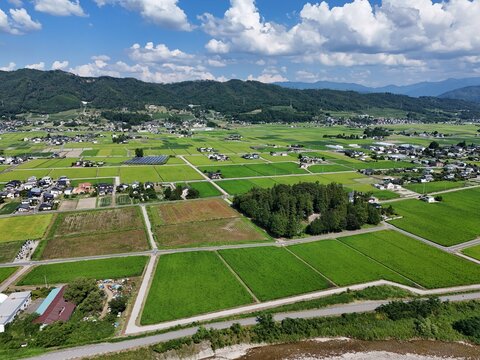 A rural area with a lot of green fields and houses. The sky is blue and there are some clouds