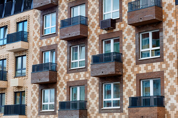 Fototapeta premium A modern residential building with a brick façade, large windows, and balconies. The brickwork is staggered, and the balconies are equipped with black metal railings.