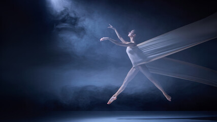 Obraz premium Ballet dancer entangled in fabric mid-motion on dark stage with spotlight. Concept of movement balance, body alignment, and dance flexibility for creative compositions.