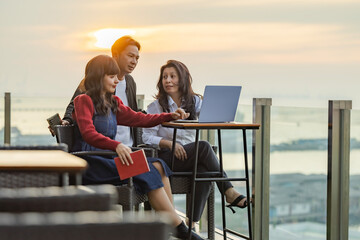 Group of Asian people enjoy each other's company, relax and talk in natural environment while sitting outdoors at on the balcony with sea view in modern hotel. Peace sunset sky, relax, summer mood.
