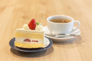 Delicious slice of cake with strawberry and a cup of coffee on a wooden table