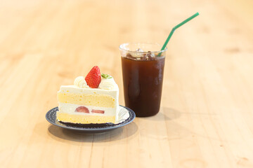 Delicious slice of cake with fresh strawberry and iced drink on wooden table in cozy cafe setting