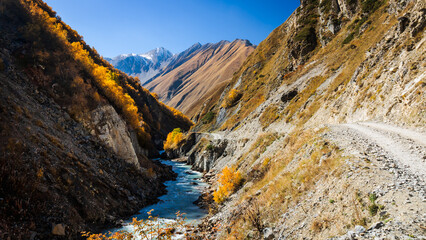 Remote dirt road winding through a golden gorge near Truso Valley in Georgia. Perfect destination for hiking, trekking and autumn travel adventures
