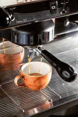 Fresh espresso streams into rustic ceramic cups from a professional machine. Close-up on the...