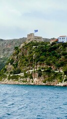 Naklejka premium Vertical photo of Kastellorizo Megisti, Greece. Ferry view of colorful houses by the sea with mountains in background. Mediterranean island, coastal landscape, summer vacation, travel, scenic seaside 